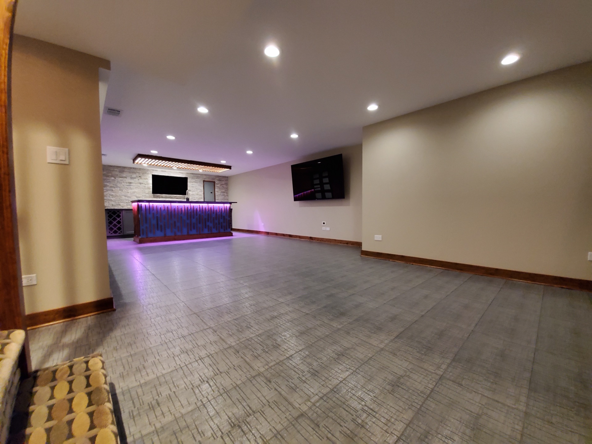 Open lounge view showing TV wall, mood-lit bar in background, and slate floor by Alpha Development Group