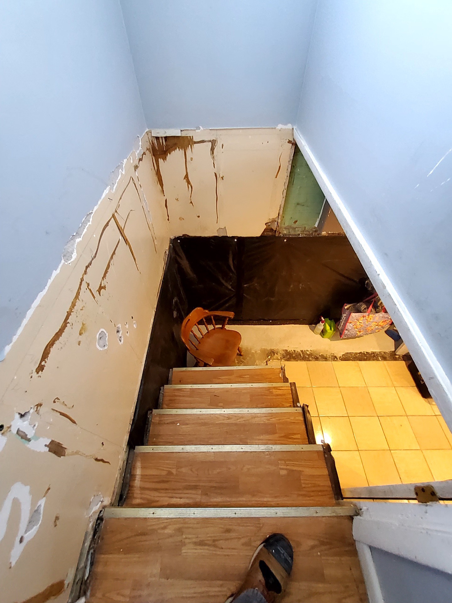 Basement stairwell before remodel: damaged drywall, exposed framing, plywood treads